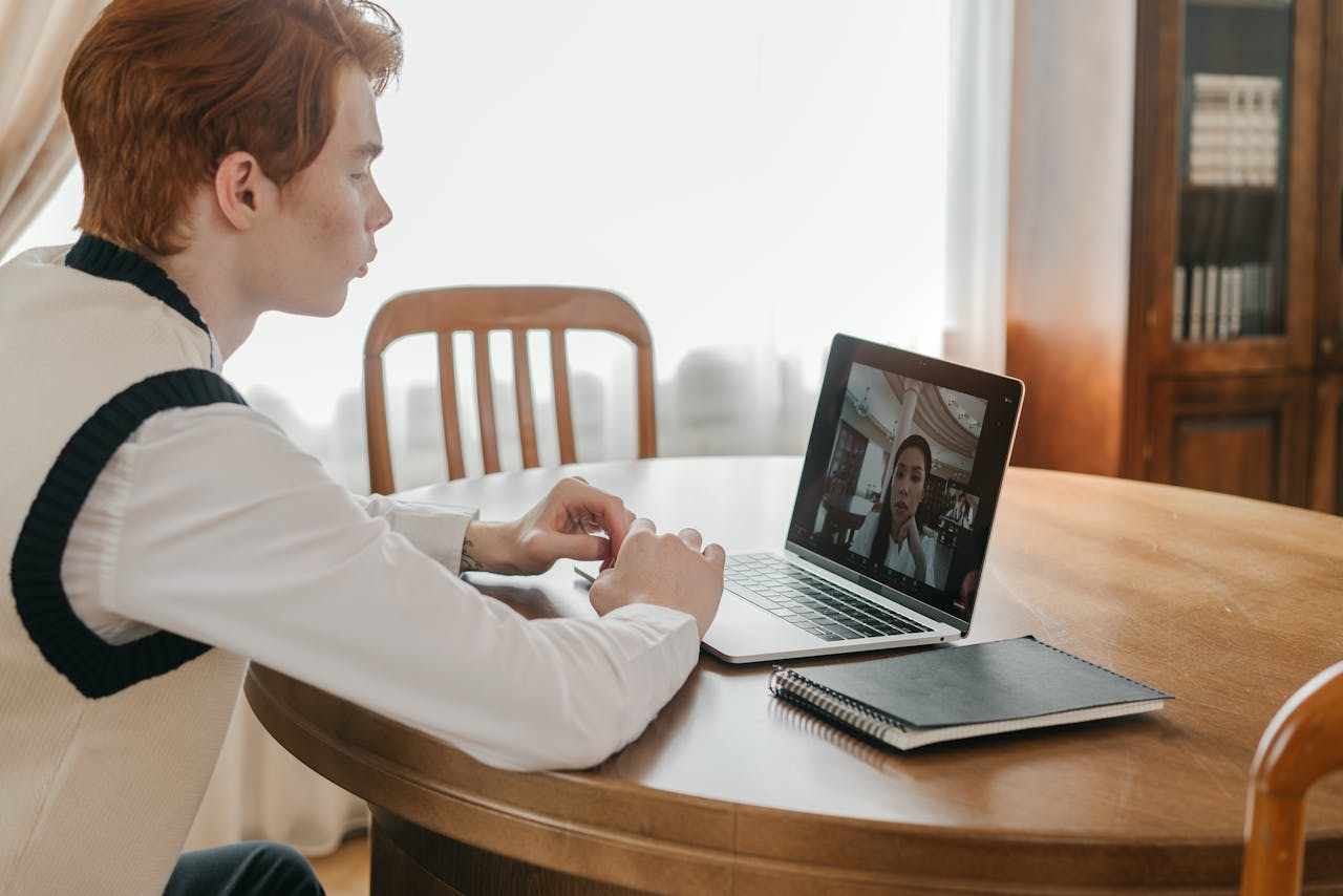 Young man engaged in a video call on a laptop at home, indicating remote communication.